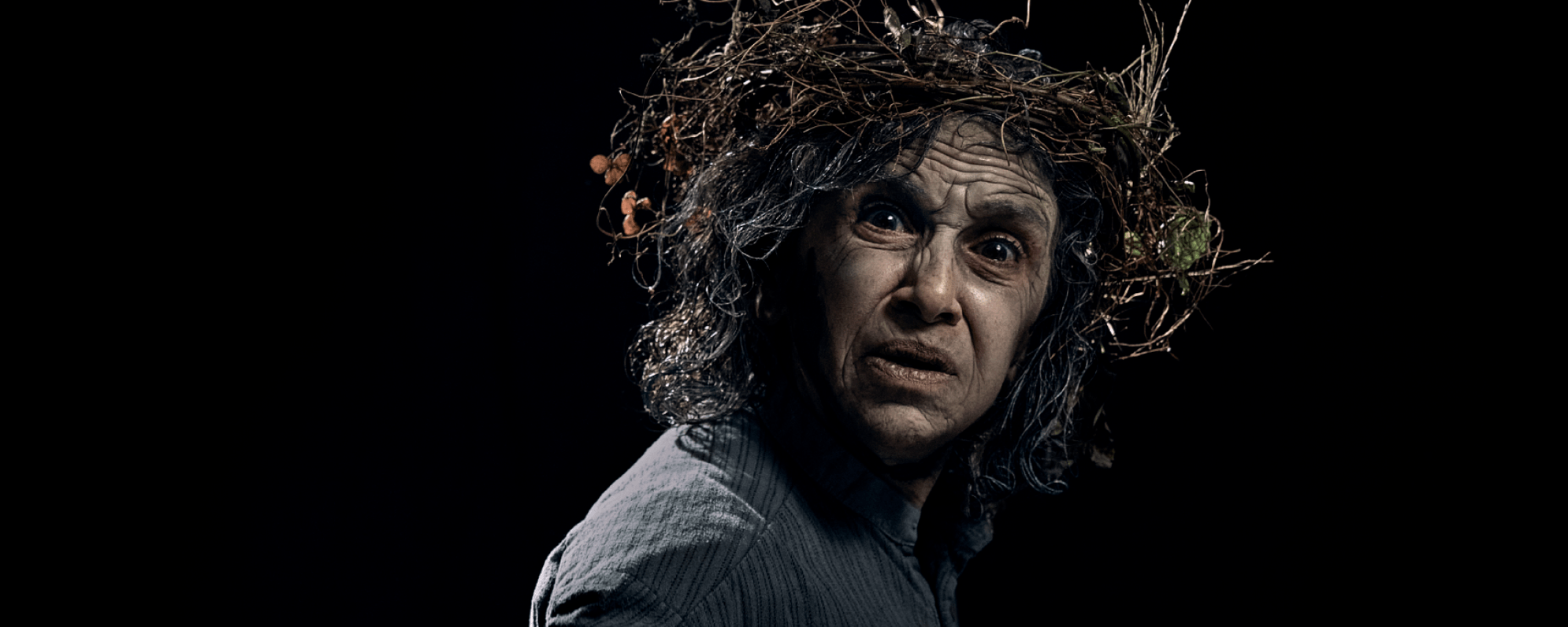 An actor with a crown of twigs looks towards the camera