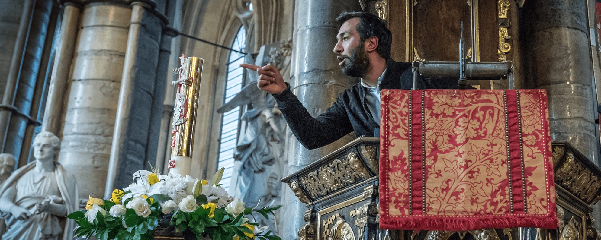 A man stands at a pulpit pointing to the right