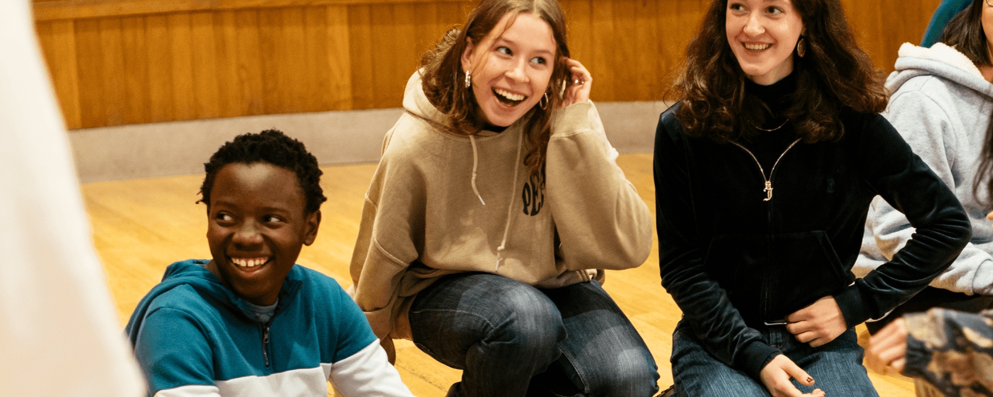 Three young people are sat, smiling widely. One of them is tucking their long brown hair behind their ear.