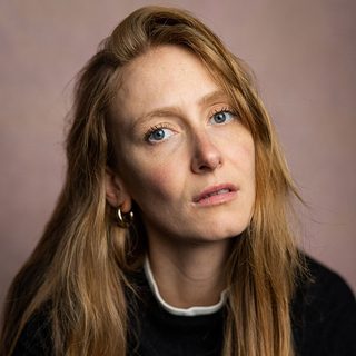 Phoebe Naughton looking directly at the camera in front of a pale pink background.