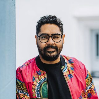 Headshot of Robin Belfield wearing a colourful jacket and glasses, looking directly at the camera.