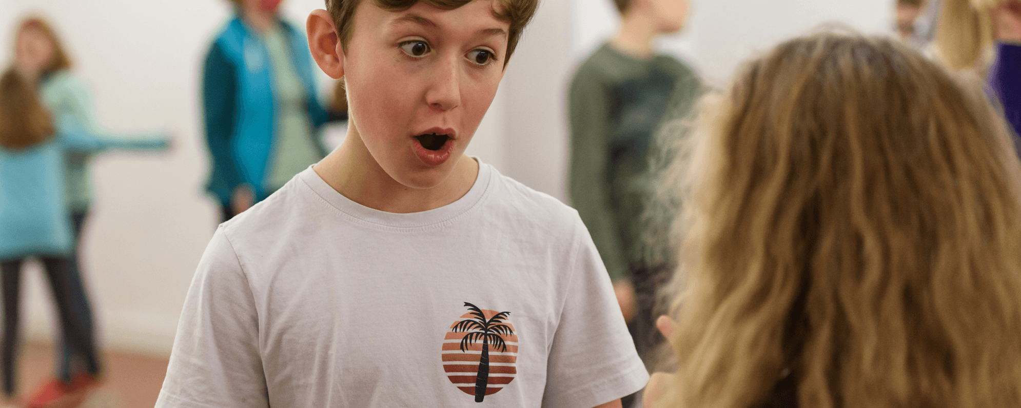 A young person with wide eyes and their mouth open looks in surprise at another person who is facing away from camera