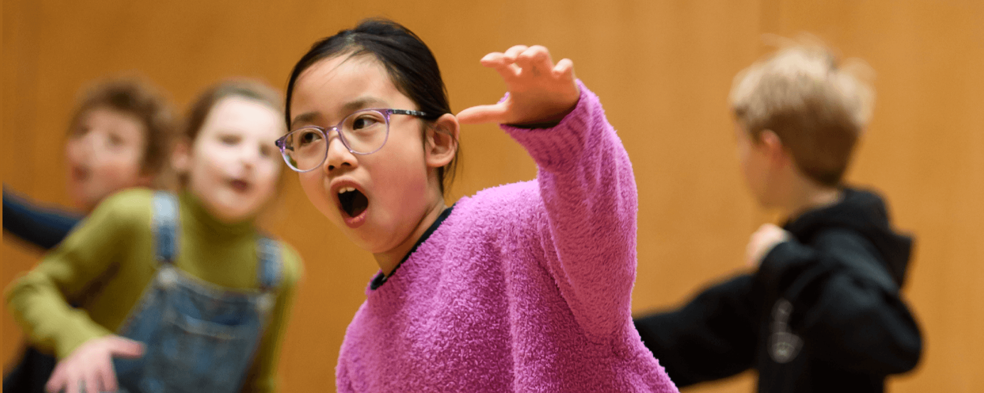 A young actor wearing glasses and a pink jumper, pretending to be an animal, roaring