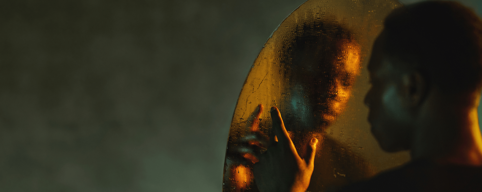 An actor looking into a mirror. The mirror is covered in water which distorts the reflection