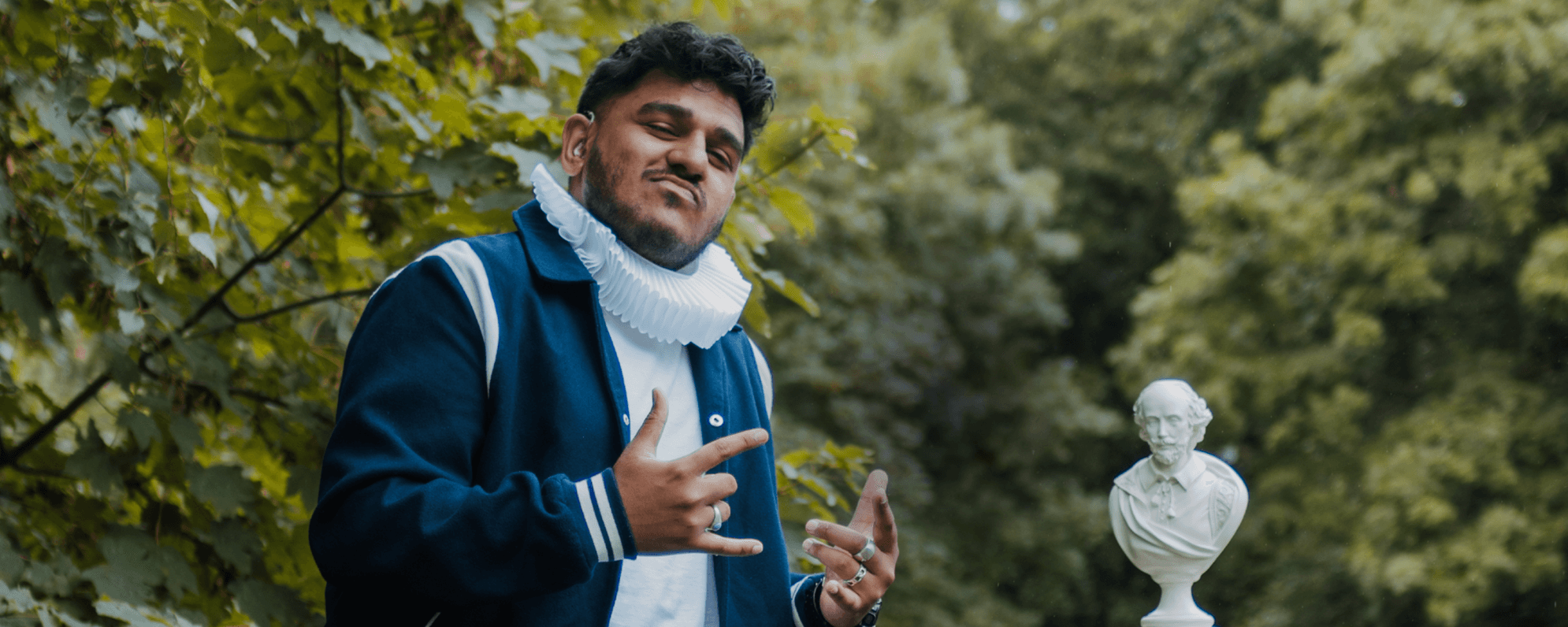 A deaf man, wearing modern clothing but with a Shakespearean ruff around his neck, gives 'hang loose' signs with his hands.