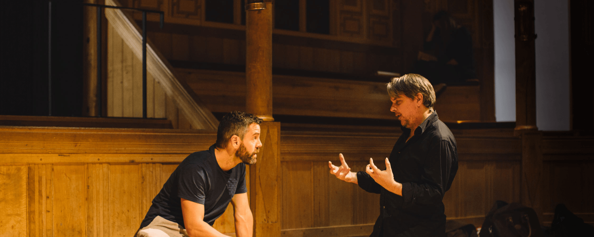 [IMAGE] Two men sitting on a wooden stage.