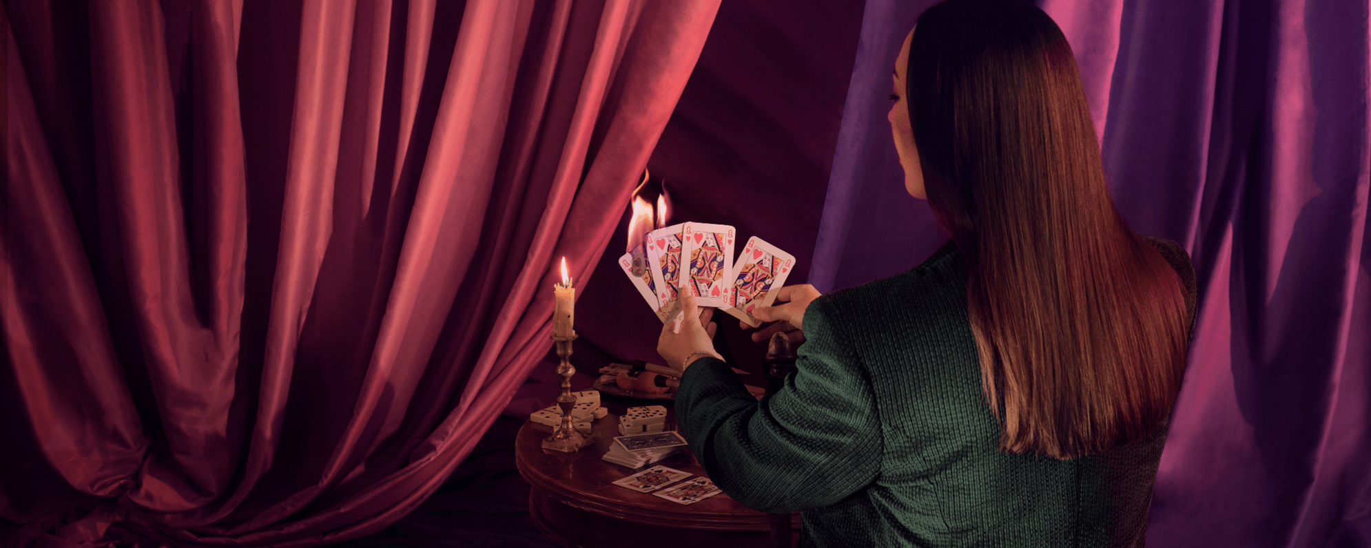 'All's Well That Ends Well' show artwork depicts a woman in a green suit sitting at a small circular table with stacks of playing cards and a single lit candle. She holds four cards, all Queen of Hearts. The card nearest the candle begins to burn.