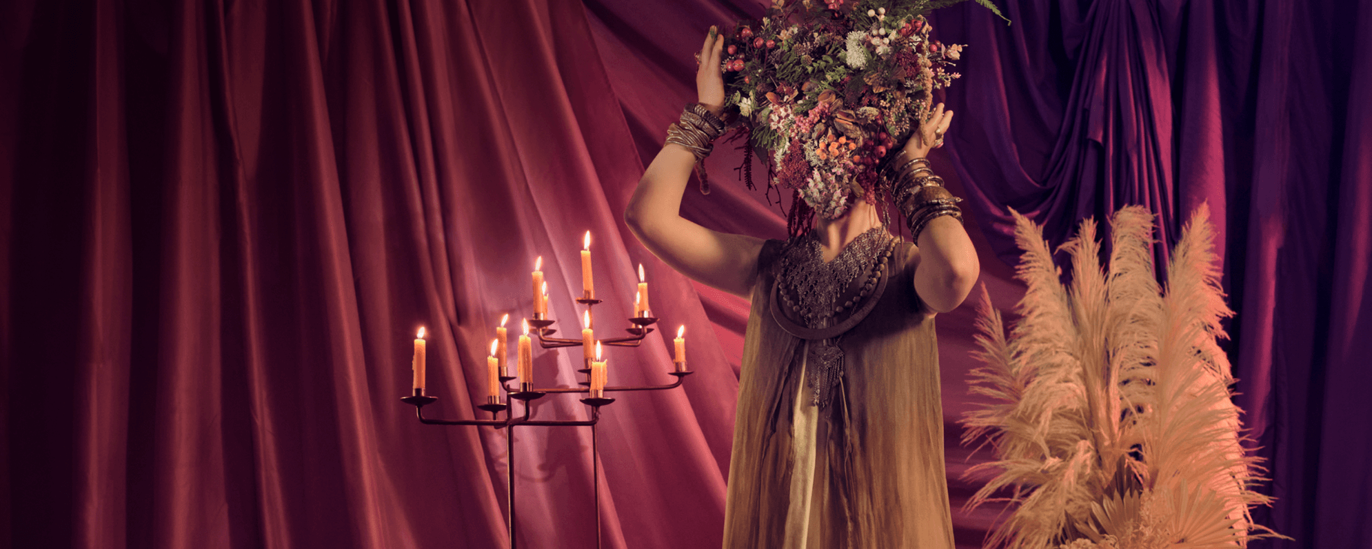 Cymbeline poster image, showing a woman with her face obscured by a floral display. She stands next to an array of lit candles.