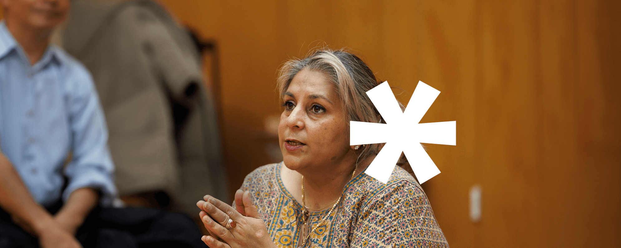 Photo of a woman mid-speech, with a white asterisk motif overlaid on top.