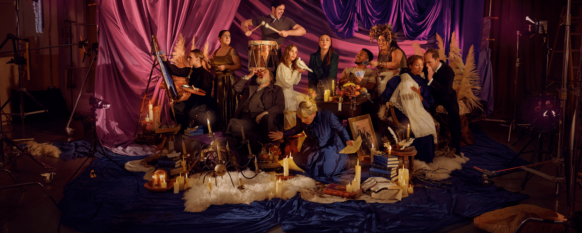 The Globe’s Winter season artwork depicts a group of characters from all the season’s shows in an energetic tableau. They are placed against a hanging backdrop of pink, purple, and blue curtains. They are surrounded by antique set dressing and many lit candles.
