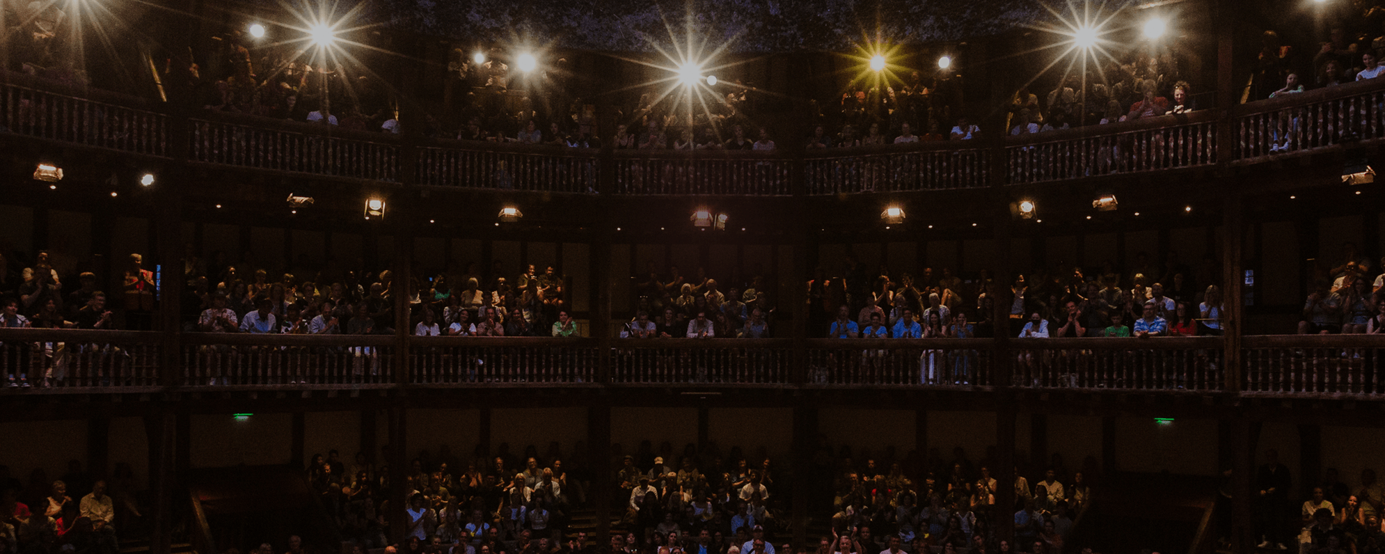 The Globe Theatre, filled with audience and bright stage lights.