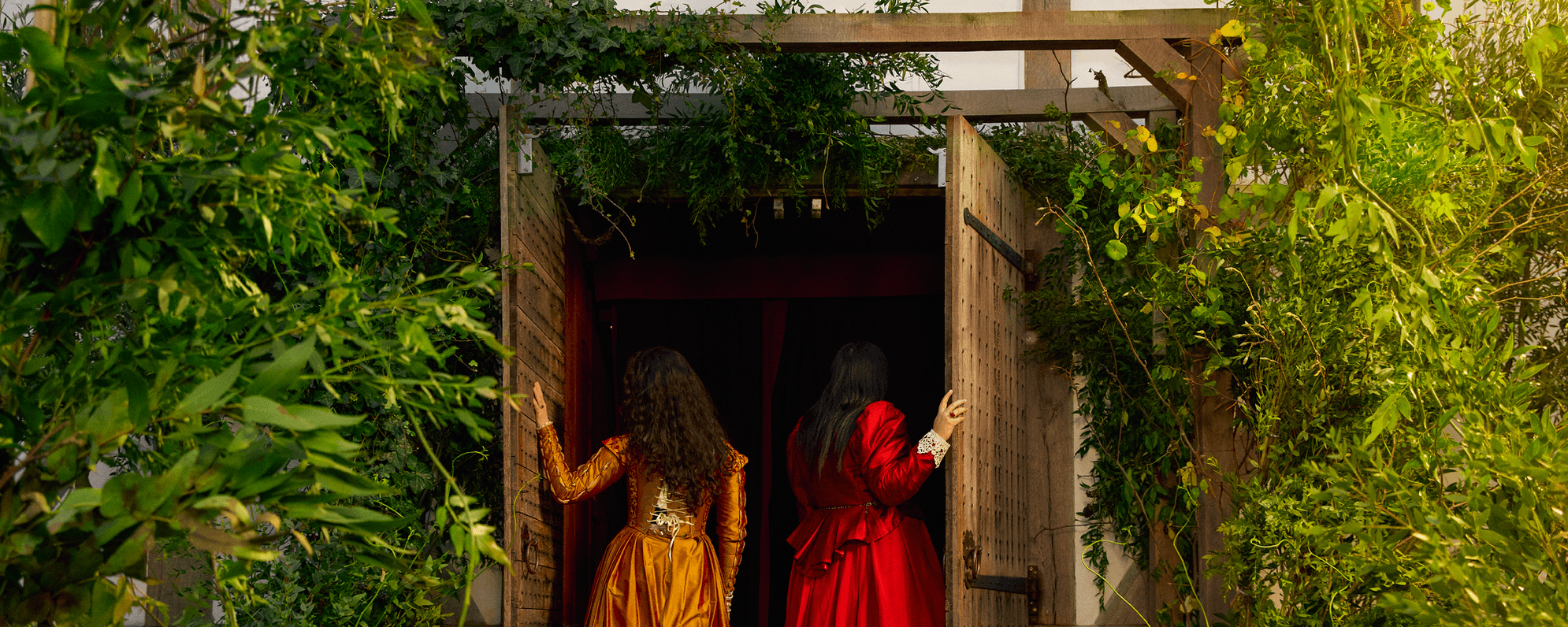 Two people in vibrant Elizabethan dresses entering the Globe