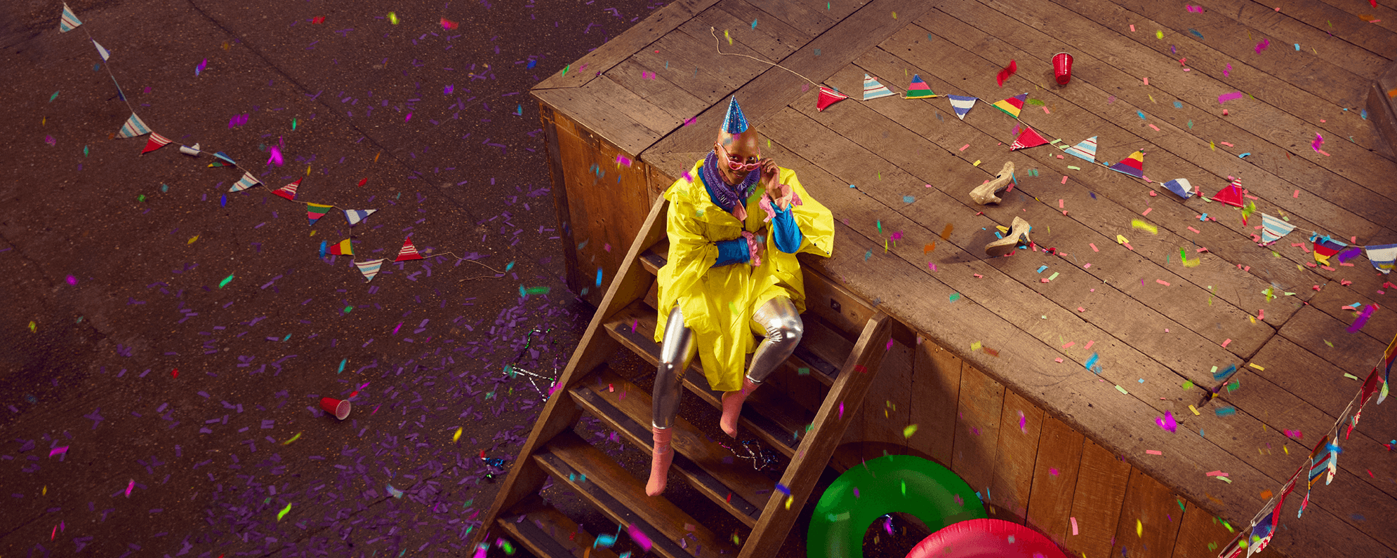 Person sat on the steps of the Globe, wearing a yellow cape and surrounded by party confetti and bunting