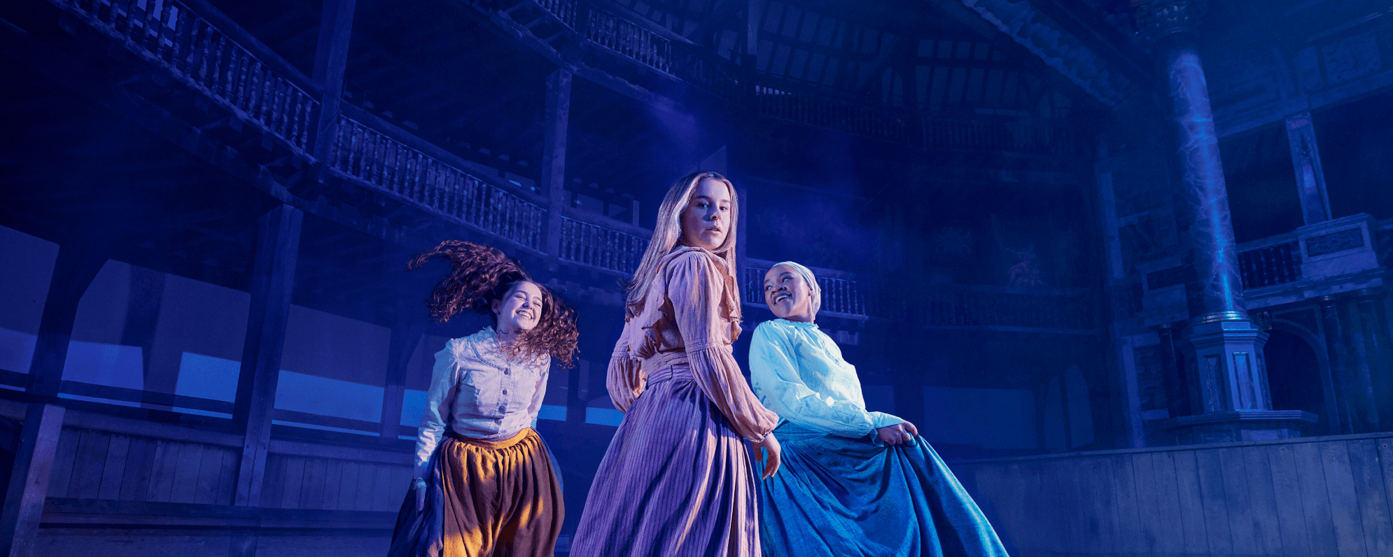 Three young women in the Globe. They're wearing period costume contemporary with The Crucible's setting - long skirts and blouses. Two of them are smiling and laughing, but the central woman looks at the camera as if shocked.