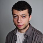 Joshua Griffin wearing a grey shirt over a white t-shirt and looking directly at the camera.
