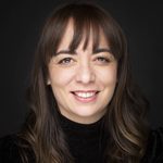 Patricia Rodriguez wearing a black turtle neck and smiling directly at the camera in front of dark background.