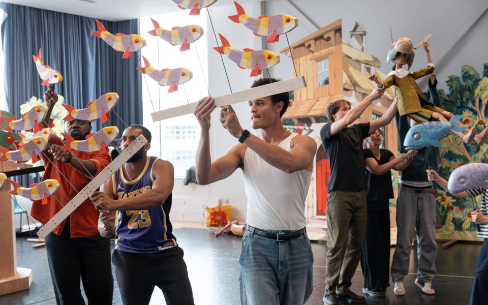 Pinocchio rehearsal image showing cast holding fish puppets aloft in a rehearsal room