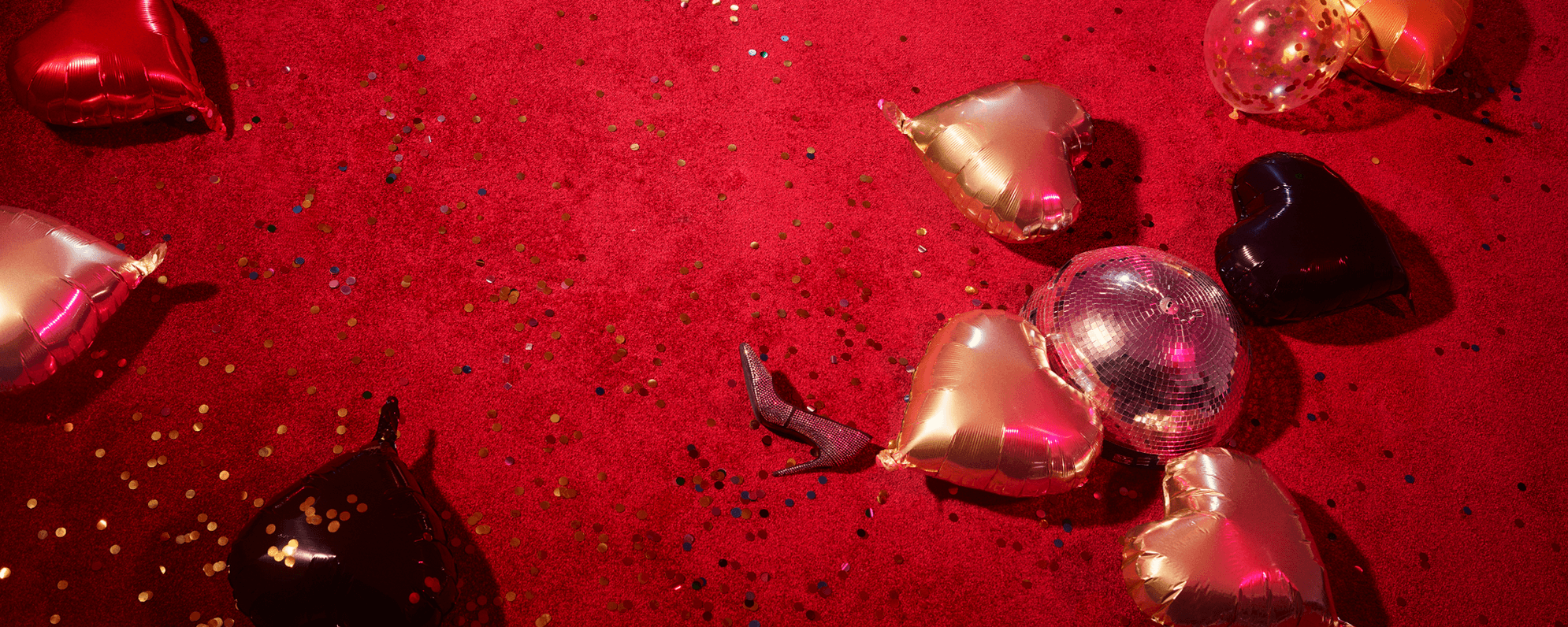 A red carpeted floor covered in glitter, heart-shaped balloons and a high heeled shoe.