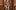 A tapestry of a person standing with their palms clasped together. They are shirtless and their chest is covered in tattoos. They wear a silver cross around their neck and baggy jeans. The tapestry has patterned edges and hangs within a wooden doorframe.