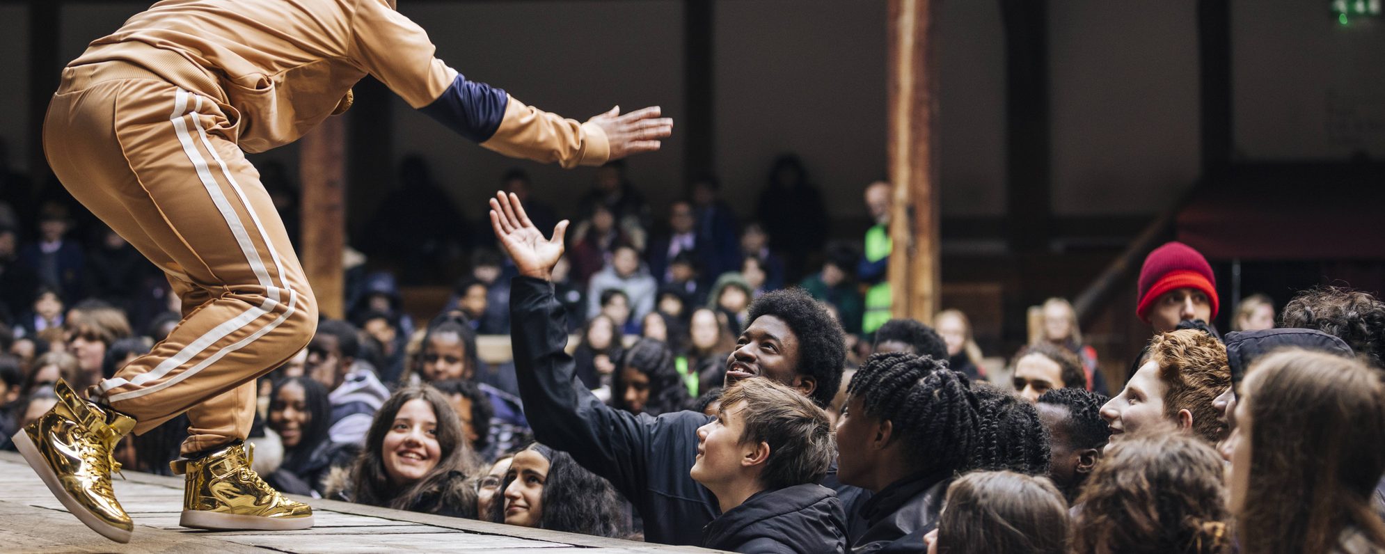 Actor running along the stage, high-fiving an audience member in the yard