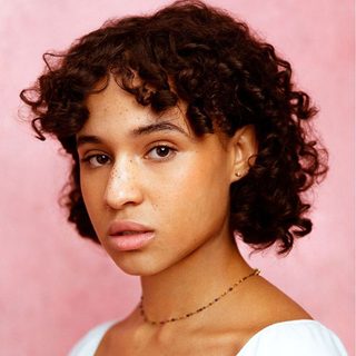 Headshot of Assa Kanouté, looking directly at the camera in front of a pink background.