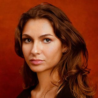 Headshot of Fia Hadeed looking directly at the camera in front of a red background.