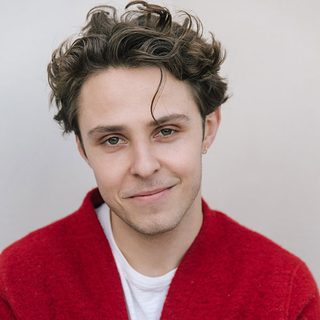 Headshot of Joseph Potter wearing a red shirt over a white t-shirt and smiling at the camera.