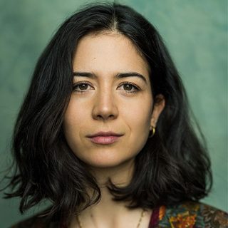 Headshot of Norah Lopez Holden, looking directly at the camera in front of a green background.