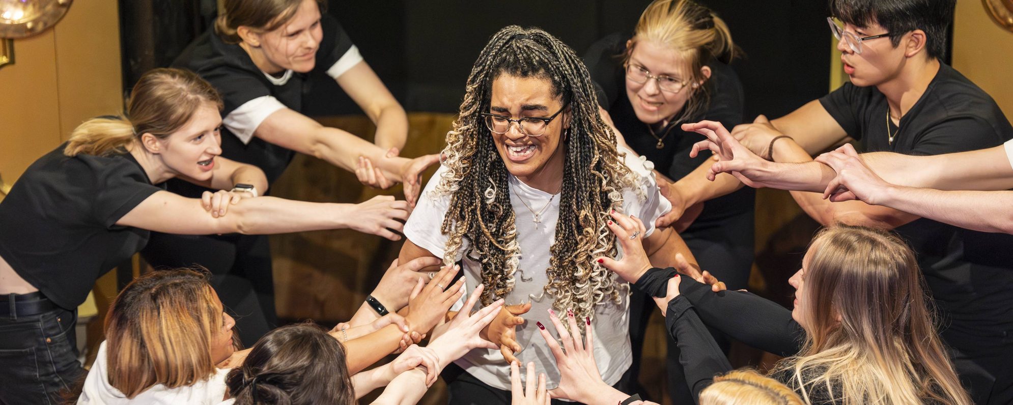 A group of Globe Youth Theatre students surrounding another student in a circle, as part of an acting exercise.