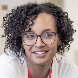 Headshot of Tinuke Craig, wearing glasses and hoop earrings.