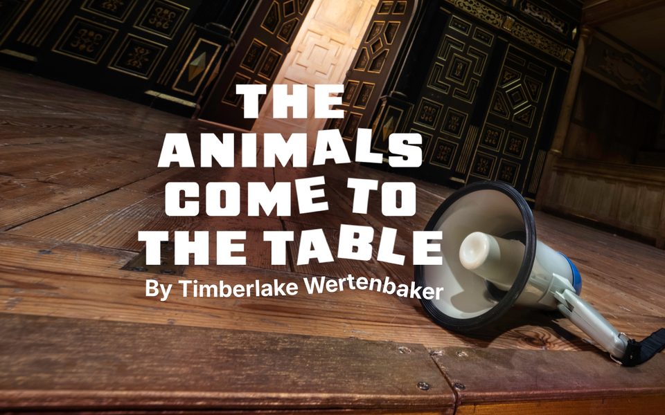 The animals come to the table by Timberlake Wertenbaker. A white and blue megaphone lies on a wooden stage. Dark wooden doors are open in the background, revealing a lighter wooden panel.