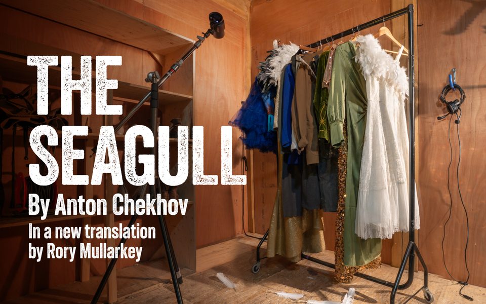 The Seagull by Anton Chekov in a new translation by Rory Mullarkey. In a wooden room, clothes hang on a rail beside a black spotlight. Headphones are also hanging on one of the walls.