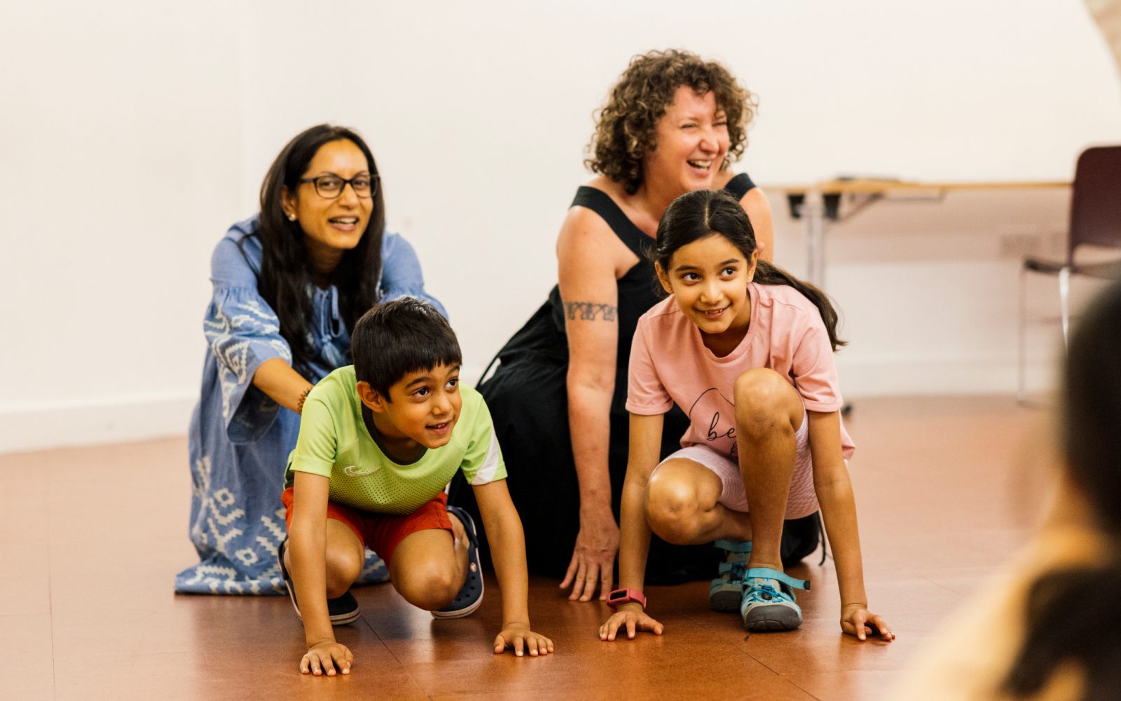 Two children and two adults are crouched down on the ground. They are all smiling.