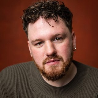 Headshot of Zachary Willis, looking directly at the camera in front of a red background.
