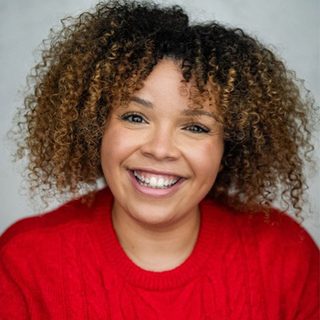Headshot of Zweyla Mitchell Dos Santos smiling at the camera, wearing a red jumper.