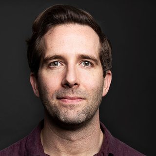 Jim Parkes looking directly at the camera in front of a dark background.