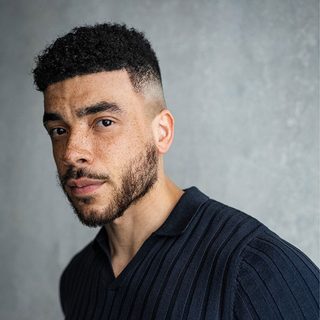 Jurell Carter wearing a navy shirt and looking directly at the camera in front of a gray background.