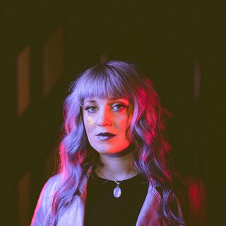 Katie Richardson lit up by a purple light and looking directly at the camera.