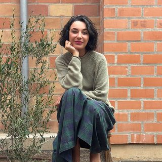 Maria Isabel Sánchez Vegara sitting down in front of a brick wall beside a plant.