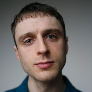 Thomas Josling looking directly at the camera in front of a grey background.