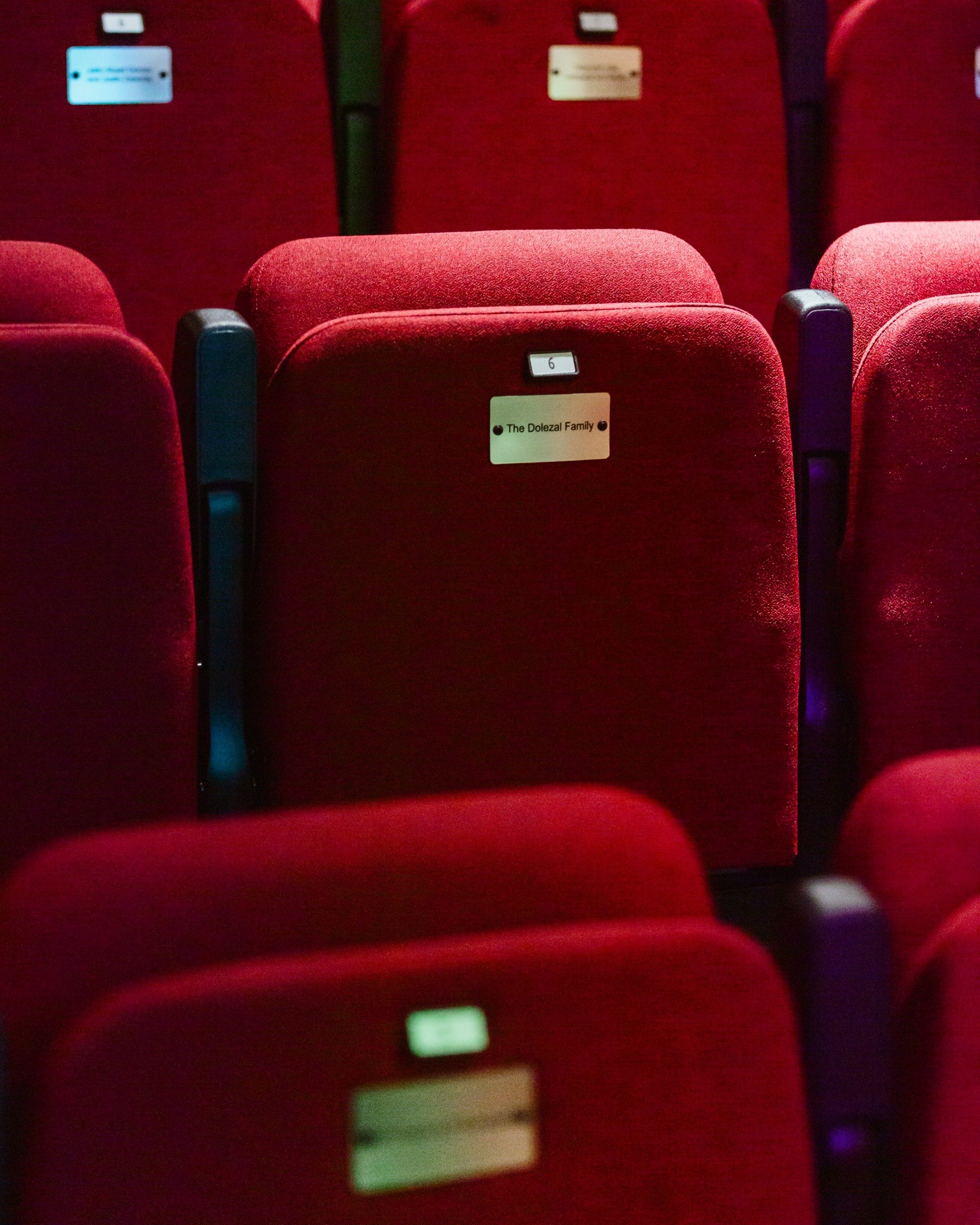 Close-up of red seats inside an auditorium with engraved names on metal plaques attached to them.